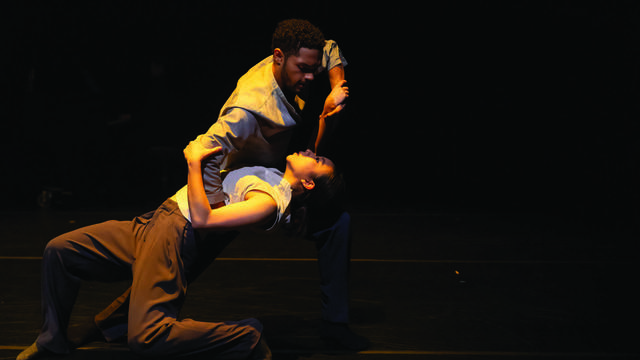 Two dancers, 在附带的标题中命名, 在昏暗的灯光下，在舞台上表演一段富有表现力的亲密舞蹈. 重点在于他们之间的紧密联系和他们动作的流畅性, 创造一个强大的和情感的表演.